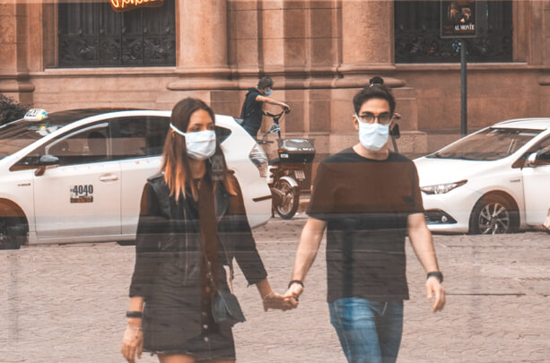 A couple walking in the street holding hands and wearing face masks.